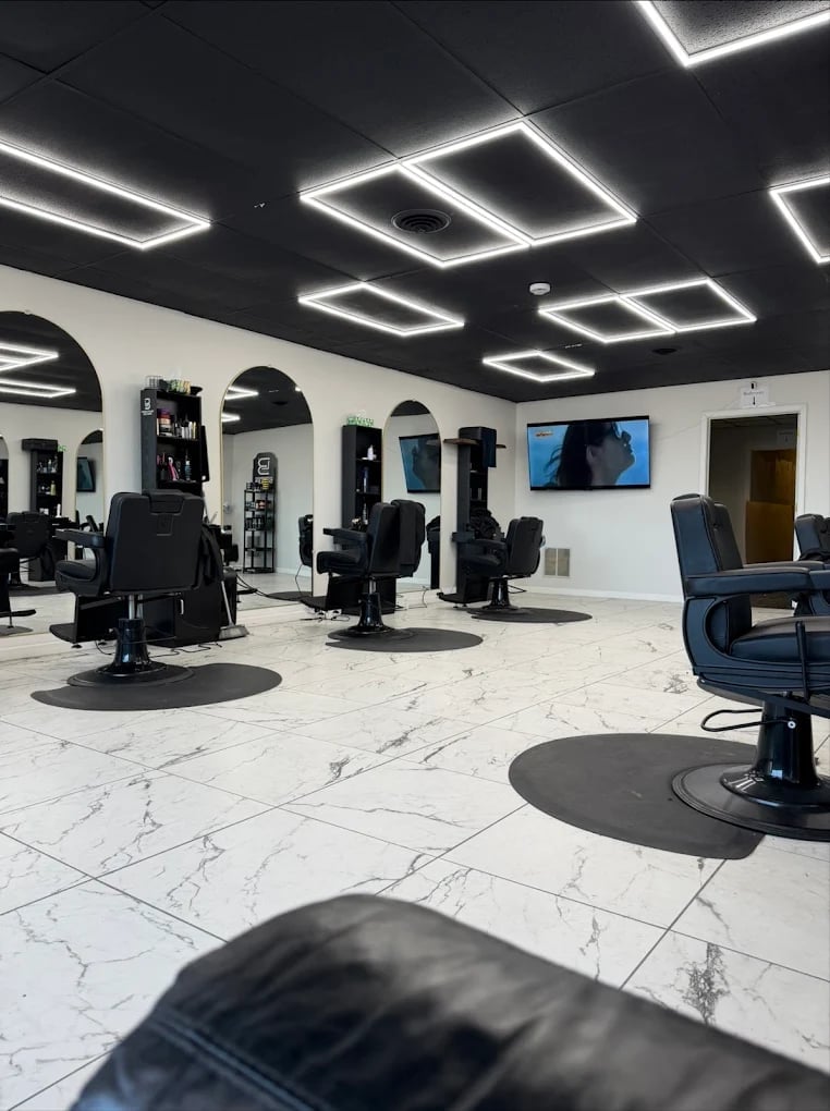 Modern hair salon interior with black barber chairs, geometric neon ceiling lights, white marble floors, and blue TV screen